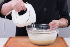 Trong một âu trộn lớn, cho kem phô mai, đường cát, nước cốt chanh và trứng gà vào đánh bông bằng máy đánh trứng.
