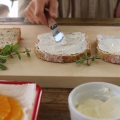 Dâu tây rửa sạch, bỏ cuống, để ráo nước và cắt làm đôi. Cam và kiwi gọt vỏ rồi cắt thành từng lát mỏng tròn. Lấy bánh mì sandwich cho lên mặt phẳng, phết một lớp kem phô mai lên trên mặt bánh.