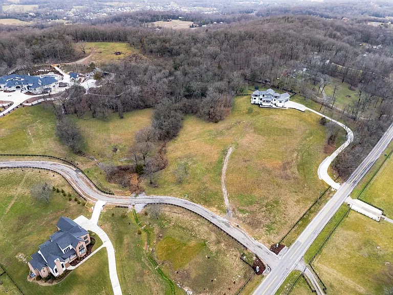 Aerial view of a large, undeveloped grassy lot in a residential area with scattered houses and wooded borders in West Tennessee.