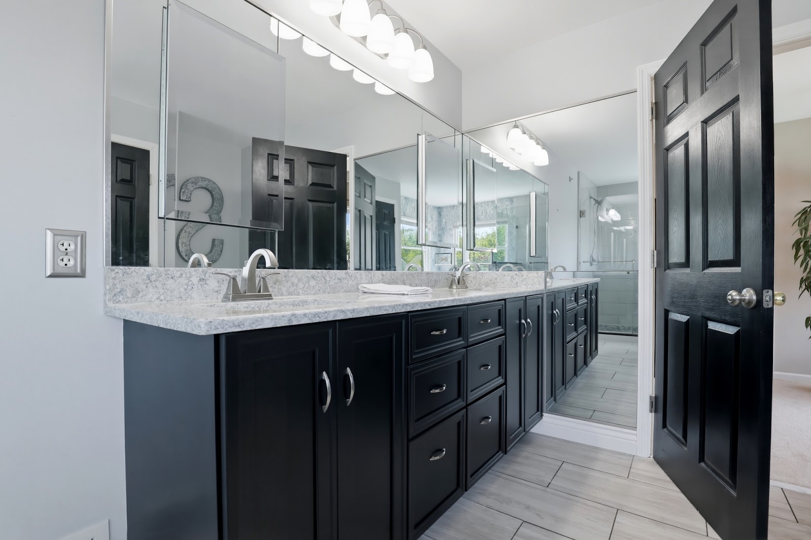 Renovated master bathroom with large double vanity, black cabinetry, quartz countertop, wide mirror with Hollywood lighting, and walk-in glass shower — South Jersey bathroom remodel by HousePro