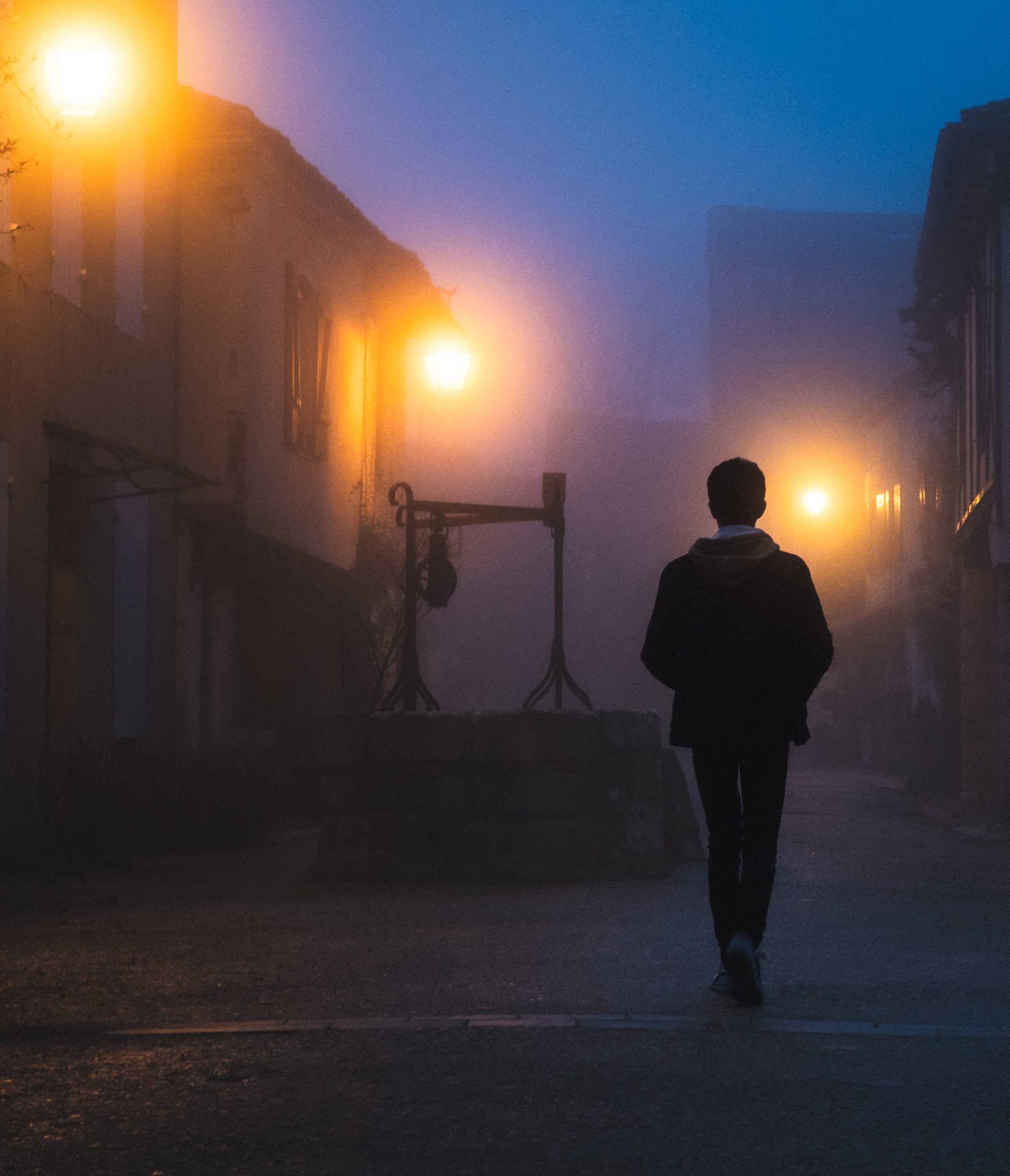 Une silhouette marche seule dans une rue noyée de brouillard.
