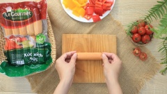 Xúc xích Đức mua về cắt thành khoanh tròn, sau đó tạo hình đẹp mắt cho xúc xích bằng cách khứa 3 đường nhỏ dọc trên thân.