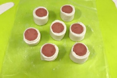 Cắt các cuộn bánh xúc xích thành những khúc đều nhau, dày khoảng 3 - 4cm. Phết lòng đỏ trứng và rắc lên lớp ngoài bột 1 ít mè trắng.