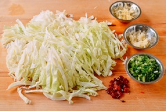 Miến cho vào tô nước ngâm 5 phút cho miến nở mềm, vớt miến ra cắt khúc vừa ăn. Bắp cải xắt sợi vừa ăn, rửa sạch, để ráo nước. Nước sốt: trộn đều 1 muỗng nước tương, 1/2 muỗng hắc xì dầu, 1/2 muỗng giấm đen, tiêu, 1 muỗng dầu mè, 1/4 muỗng đường và 115ml nước trong chén.