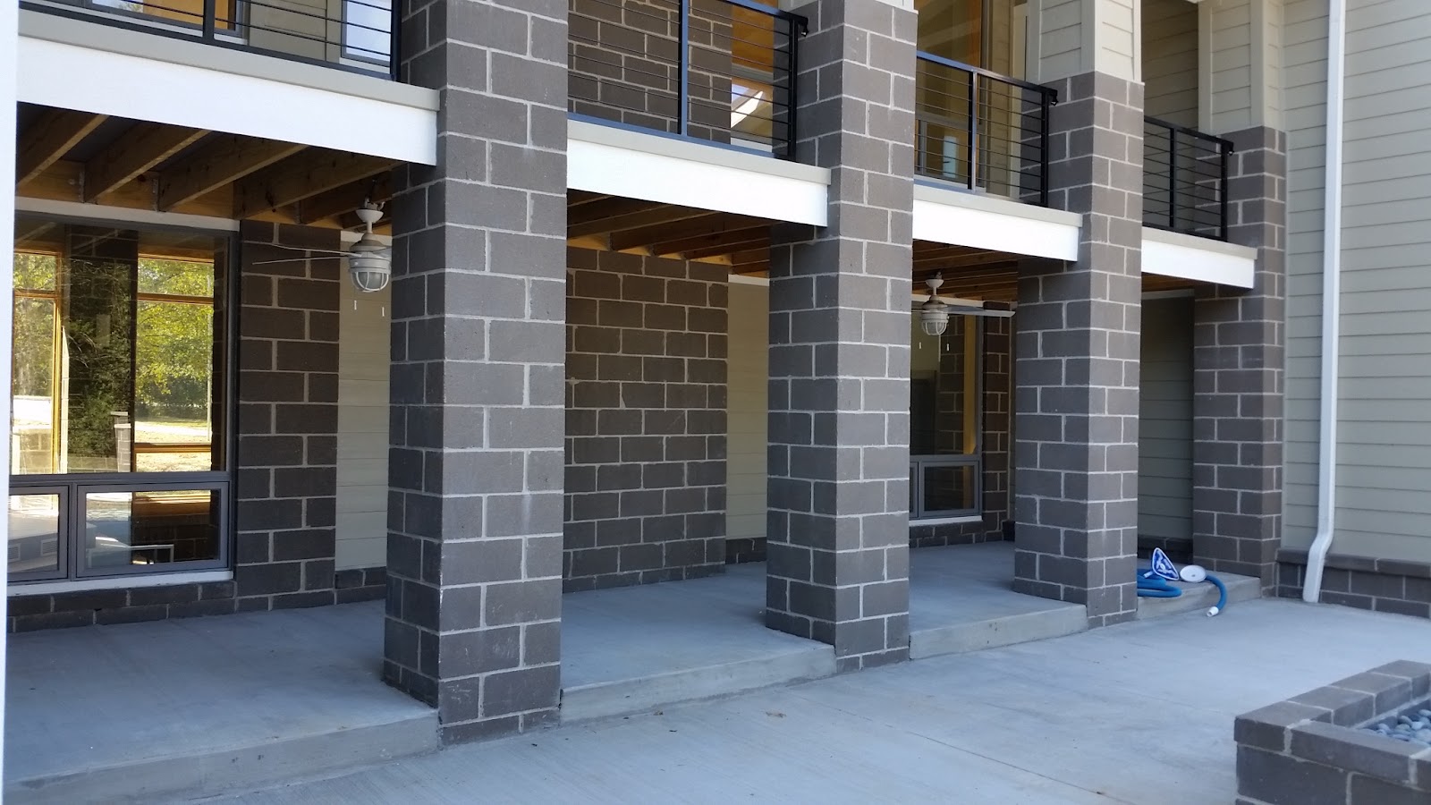 Outdoor patio area featuring grey block support pillars, concrete flooring, and an upper-level balcony with black metal railings.