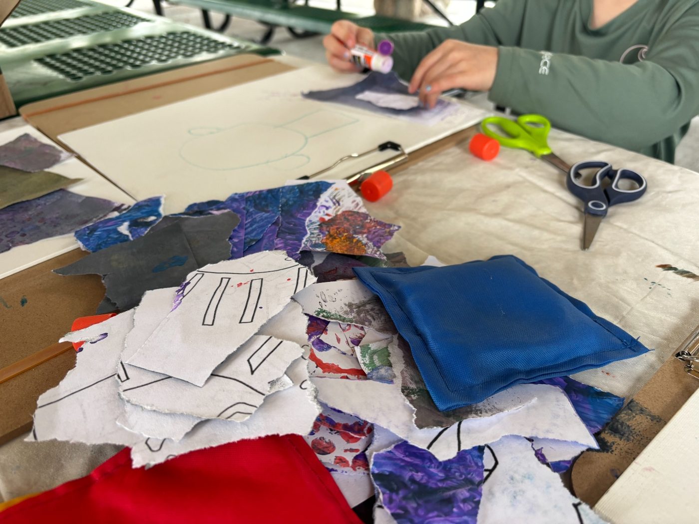 A student's hands applying glue to torn painted paper pieces for a collage