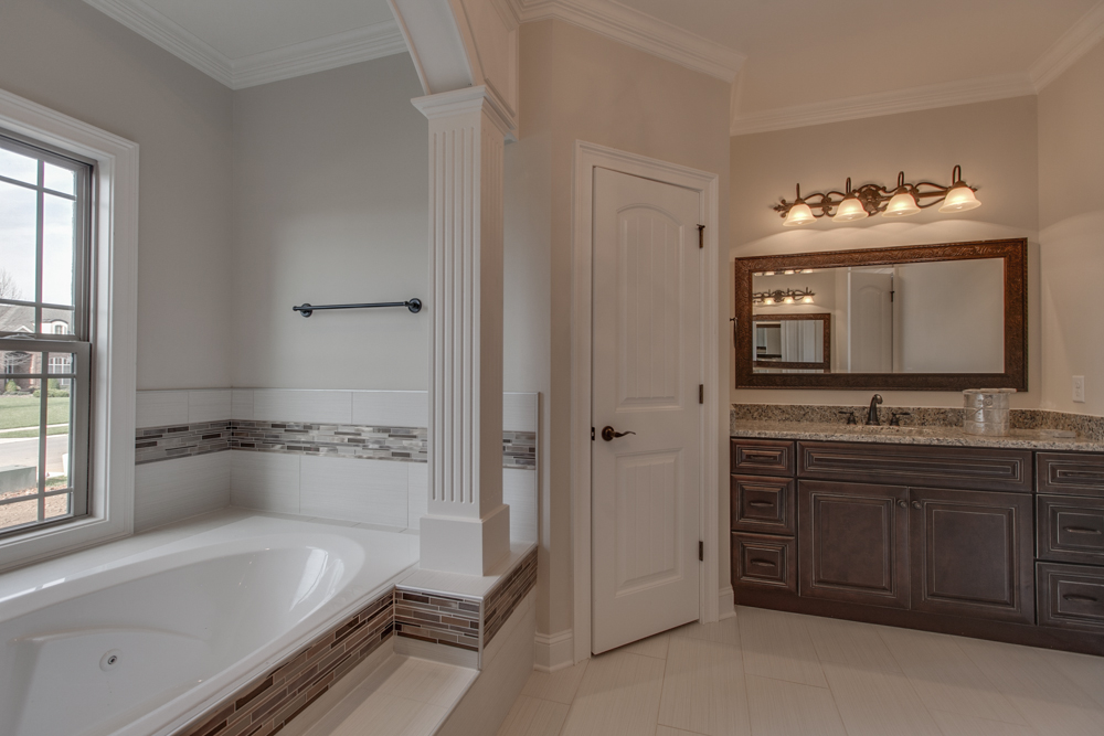 Bathroom interior showing a built-in bathtub with tile surround next to a window, a white door, and a dark wood vanity.