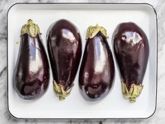 Mở lò nướng trước ở 205 độ C. Trong chén nhỏ, trộn đều 2 muỗng dầu olive, tỏi băm, 1/2 muỗng gia vị thảo mộc Ý, 1/4 muỗng muối rồi khuấy cho tan đều. Cà tím rửa sạch, để ráo nước và cắt đôi, dùng dao khứa hình caro trên mặt cà. Sau đó đặt cà lên khay, phết nước sốt lên cà rồi úp xuống và cho vào lò nướng khoảng 60 phút cho cà chín mềm, có màu vàng nâu.