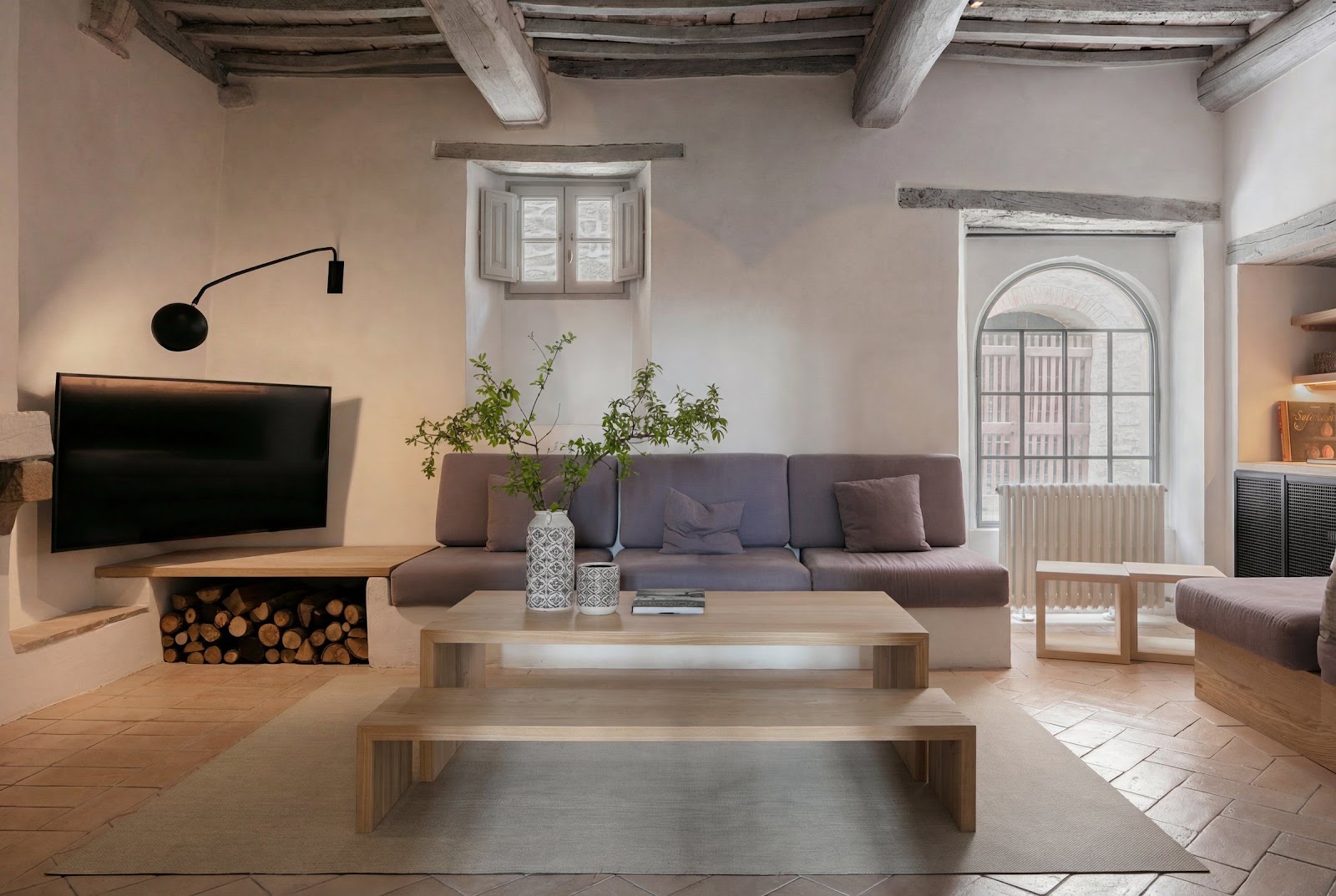 A living room with a beamed and vaulted ceiling, stone fireplace and pale walls in a restored Tuscan house