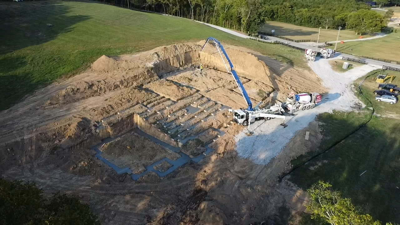 Aerial view of the Brookland construction site during foundation pouring, showing heavy machinery and excavated earth in a rural setting.