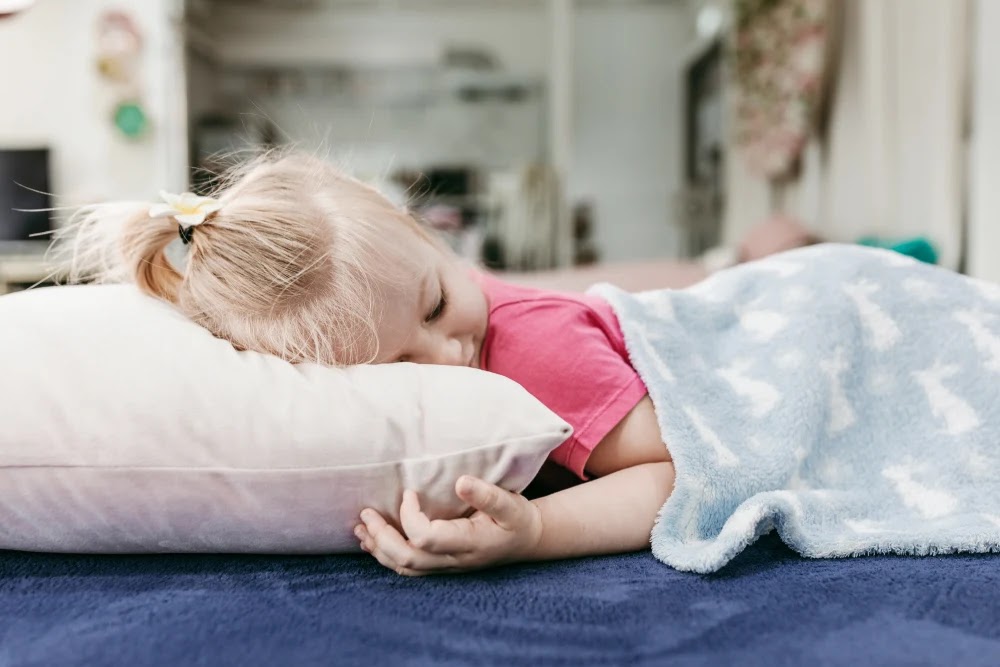 طفل صغير يأخذ قيلولة على وسادة تحت بطانية على سجادة ناعمة كحلية لغرفة الطفل