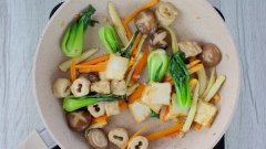 Bắc lên bếp một chiếc chảo sạch, làm nóng 2 muỗng canh dầu ăn, cho 20gr hành boa rô cắt lát vào phi thơm. Sau đó cho đậu hũ và mì căn vào xào 5 phút. Tiếp theo cho hết các loại rau củ vừa trụng vào chảo, thêm thêm 2 muỗng canh hạt nêm chay, xào nhanh tay ở lửa lớn cho rau củ nóng lên và thấm gia vị.