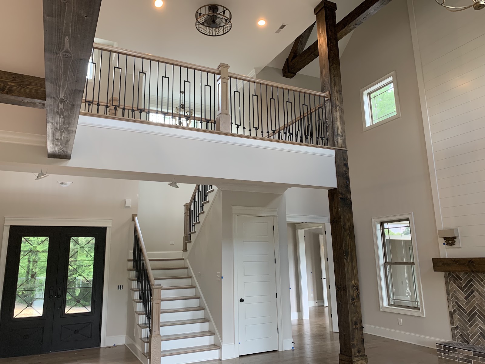 Interior view of a home foyer featuring a high ceiling with dark wood beams, a staircase, and a second-floor balcony with metal railings.