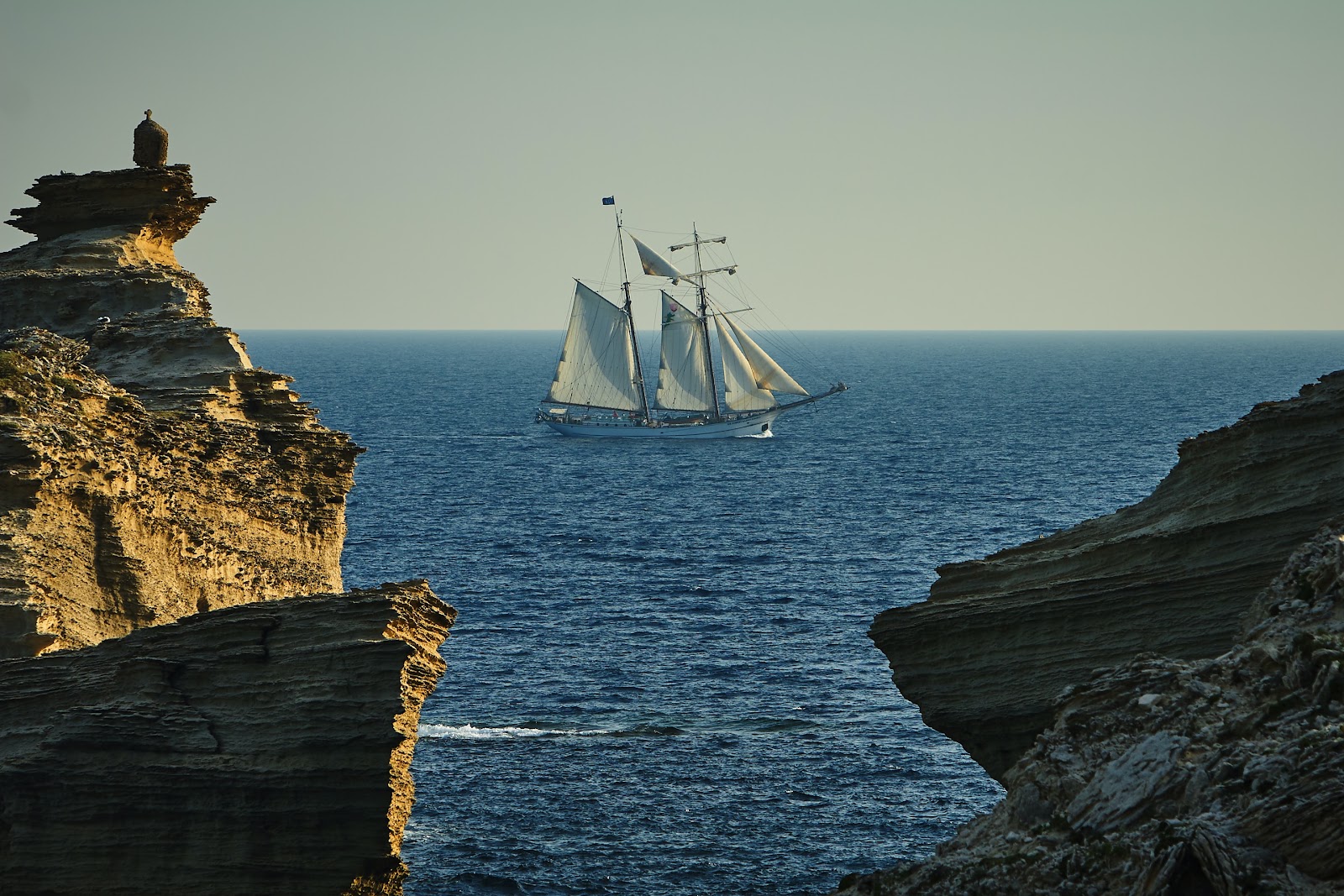 Coastal wind-eroded rocks overlooking a Galleon ship sailing in the sea on the horizon