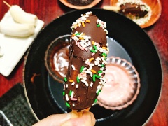 Cho chocolate đen và chocolate vị dâu + chocolate trắng ra 2 bát riêng biệt, đem đun cách thủy và khuấy đều cho chocolate tan chảy hết là tắt bếp. Lấy kem chuối trong tủ lạnh ra và nhúng vào bát chocolate đã đun tan chảy, tùy theo vị mà bạn thích. Nhanh tay rắc cốm cốm màu lên trên kem chuối, cứ như vậy bạn làm cho hết chỗ kem chuối còn lại. Cất vào tủ lạnh khoảng 1-2 tiếng đồng hồ là có thể dùng.