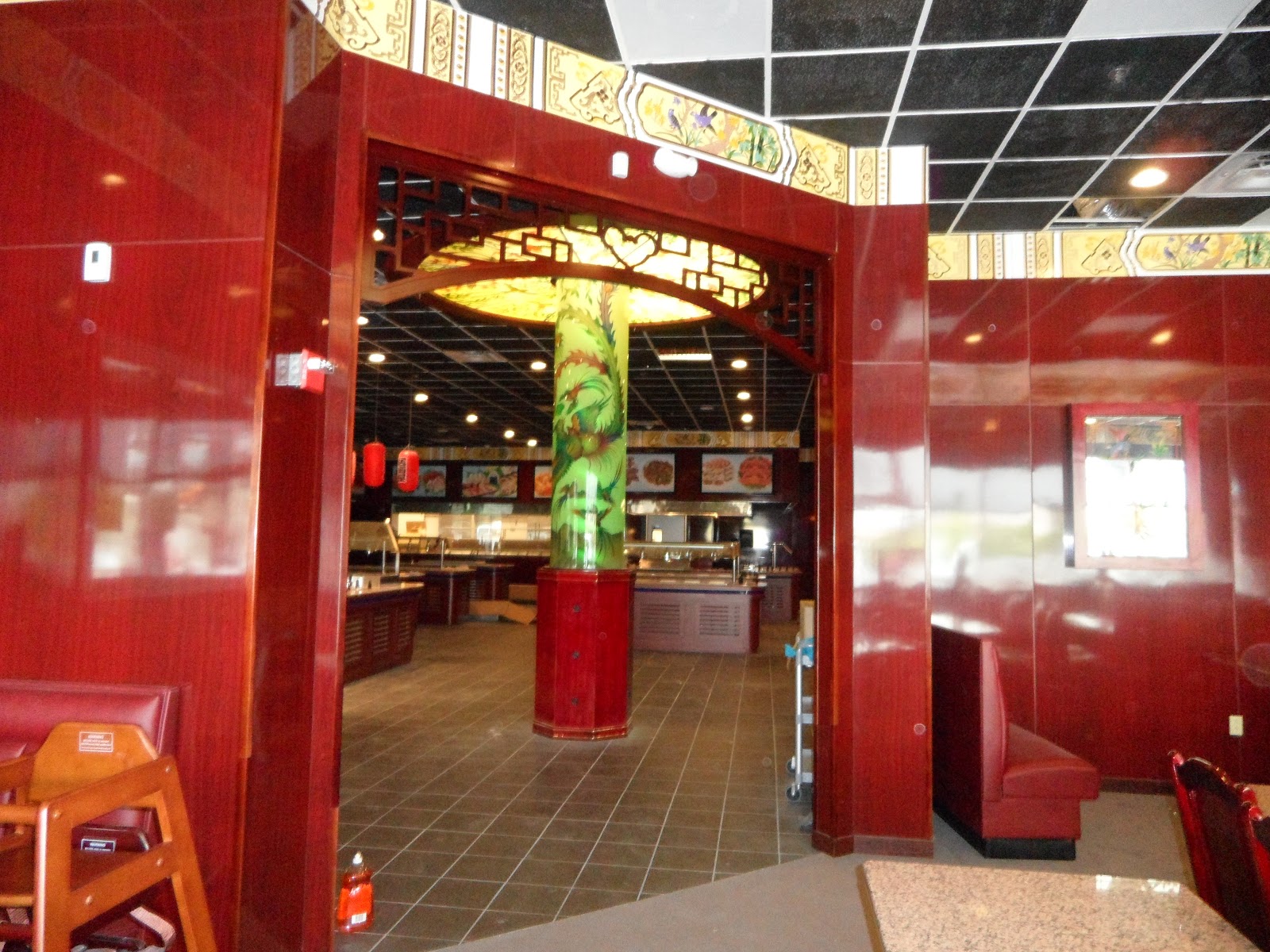 Interior view through a red paneled doorway showing a central pillar decorated with a green dragon motif under a circular light fixture.