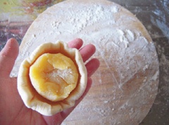 Ngắt bột bánh bao thành từng miếng nhỏ, vo tròn, ấn dẹp, cho nhân trứng gà vào giữa rồi vo tròn lại.
