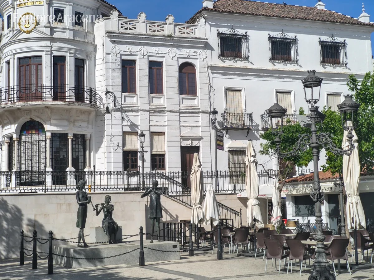 Plaza in Aracena with musician statues, café seating, and a historic building with a clock tower.