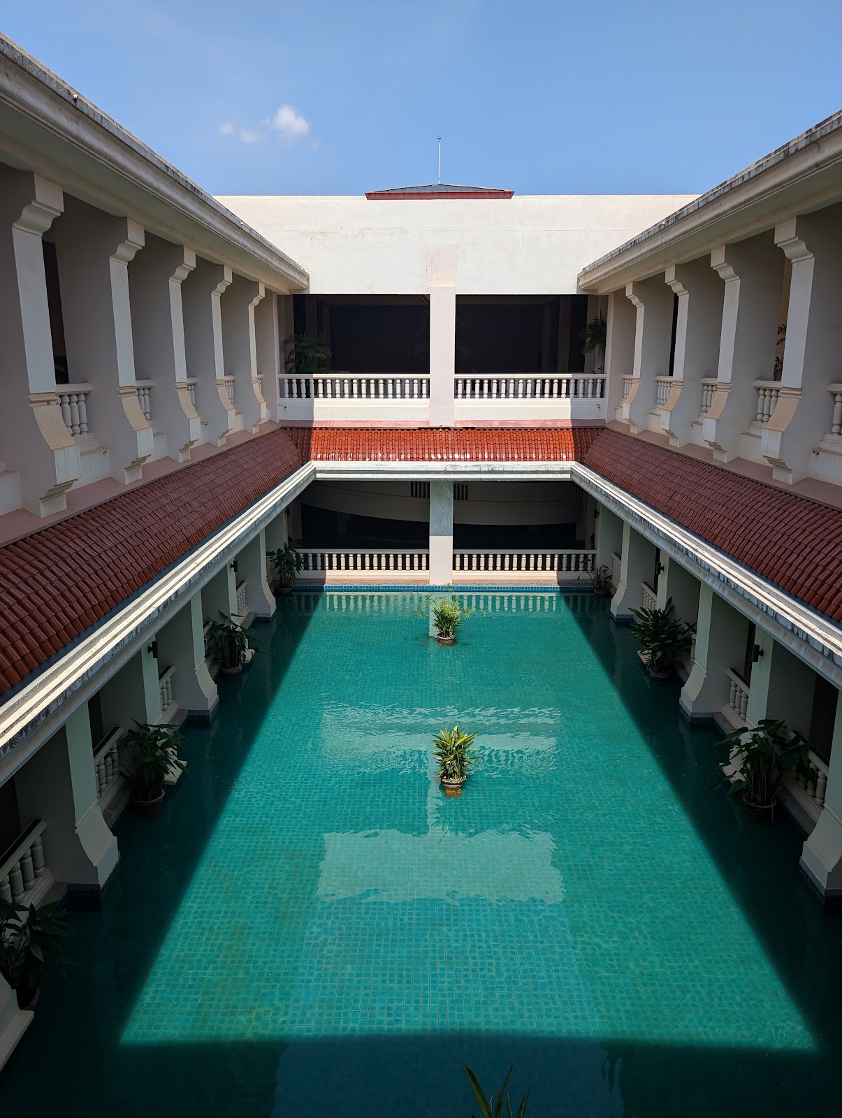 A view from a second floor balcony of a courtyard with a
                 turquoise pool below a blue sky