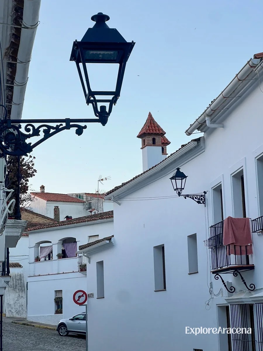 A narrow street between whitewashed houses in Aracena, with a traditional hanging lantern suspended between the buildings.