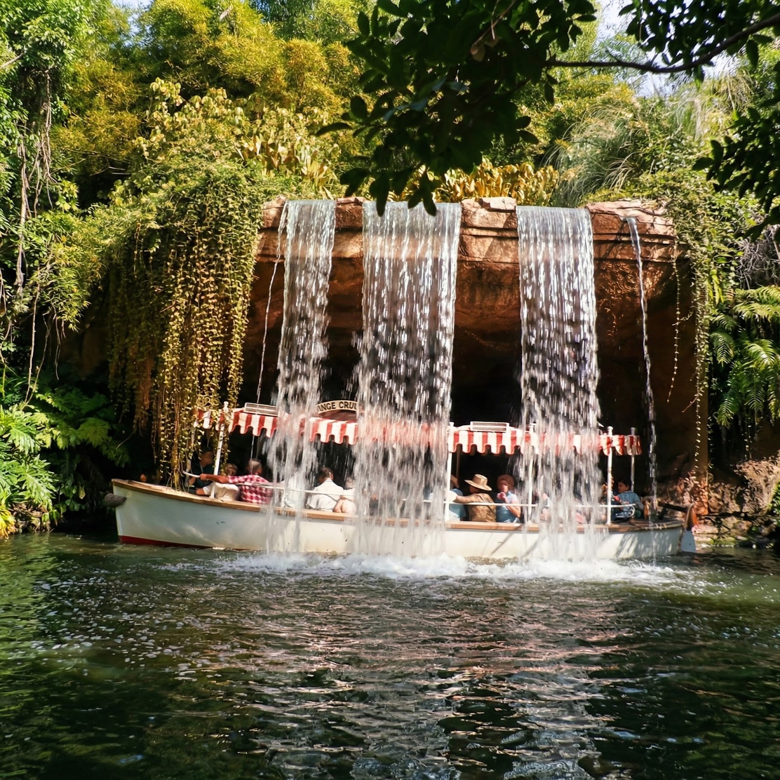 Jungle Cruise riverboat with white hull, red trim, and red-and-white striped canopy passing near Schweitzer Falls waterfall at Walt Disney World's Adventureland