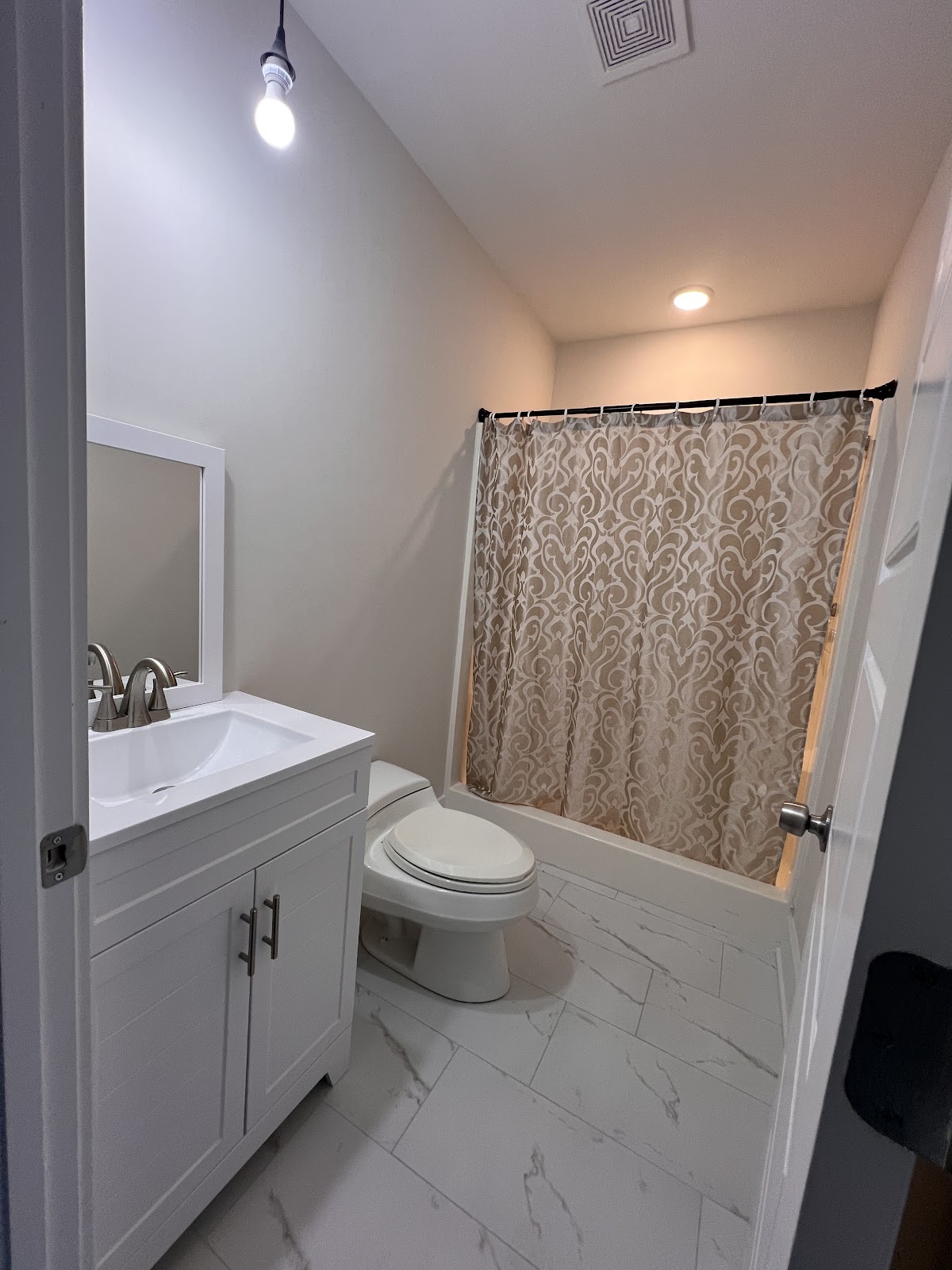 Finished bathroom featuring a white vanity, a white toilet, marble-patterned floor tiles, and a shower with a tan and white patterned curtain.