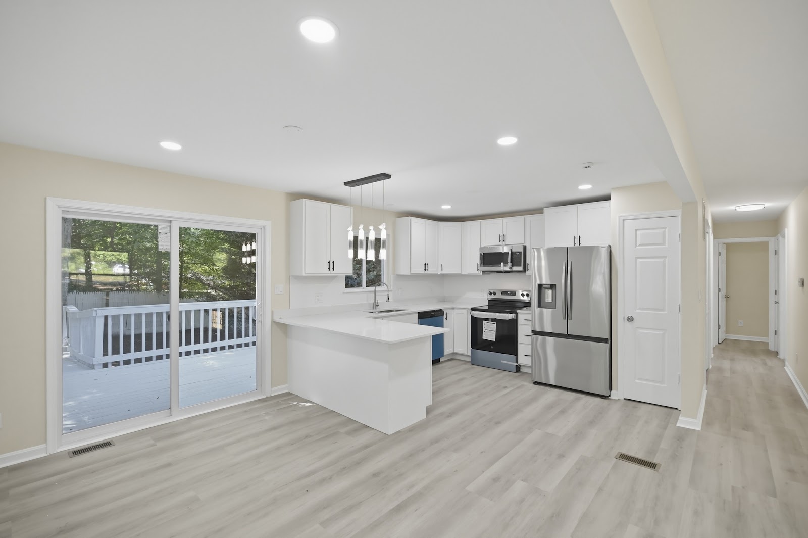 Modern white kitchen with peninsula, stainless appliances, pendant lighting, and sliding glass door opening to a back deck — South Jersey kitchen renovation