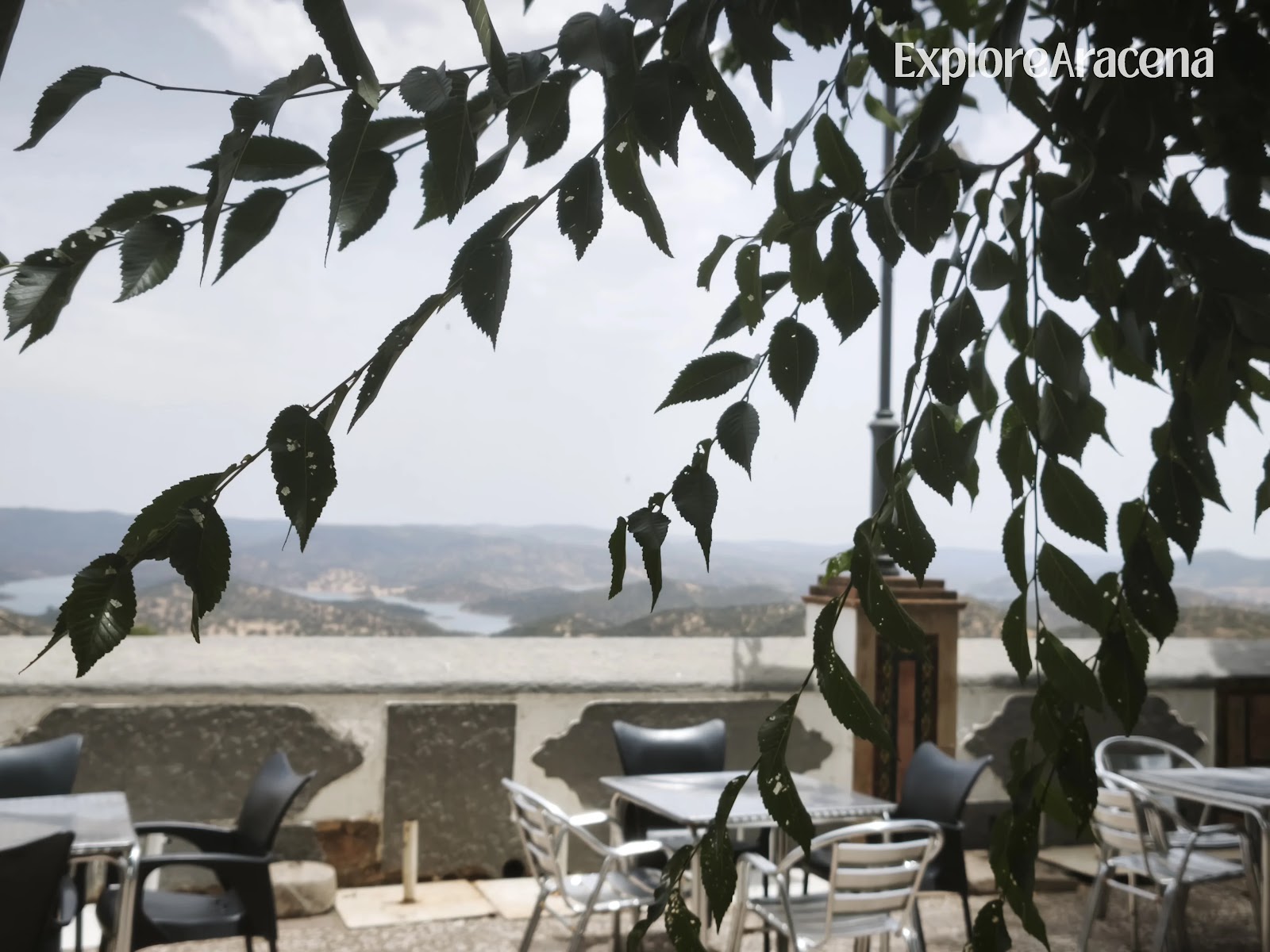 Outdoor restaurant tables overlooking the Sierra and Zufre reservoir, framed by tree branches in the foreground.