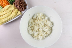 Vậy là đã chuẩn bị xong phần rau củ, trứng và thịt bò, bây giờ sẽ chuẩn bị phần cơm. Cho vào cơm nóng 1/2 muỗng cà phê muối, 1/2 muỗng cà phê tiêu, 1/2 muỗng cà phê đường, 2 muỗng cà phê dầu mè, 2 muỗng cà phê mè rang, trộn đều.