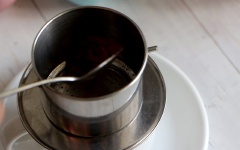 Cho vào phin 2 muỗng cà phê, dùng gạt ép cà phê vừa phải, không quá chặt cũng không quá lỏng. Đầu tiên bạn rót vào 20ml nước sôi, để khoảng 15 giây cho cà phê ngấm rồi tiếp tục cho 60ml nước sôi còn lại. Đậy nắp phin và chờ cà phê rơi xuống đến khi hết nước.