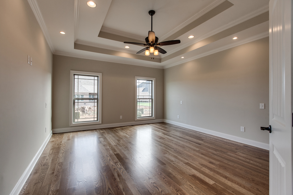 Bedroom with hardwood floors, tan walls, and a tray ceiling featuring a dark wood ceiling fan.