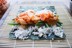 Đặt mành tre lên trên một bề mặt phẳng, trải 1 lá rong biển lên trên mành tre, sau đó múc cơm vào, dàn đều. Cho hành lá và kim chi cải thảo vào, dùng tay cuốn chặt cuộn cơm lại. Làm lần lượt với những lá rong biển còn lại cho đến khi hết.