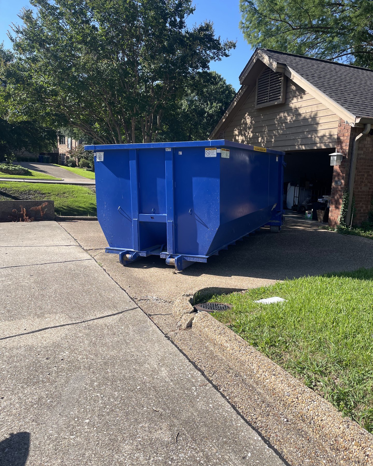 15 yard roll-off dumpster by an open garage for a cleanout in Sachse area