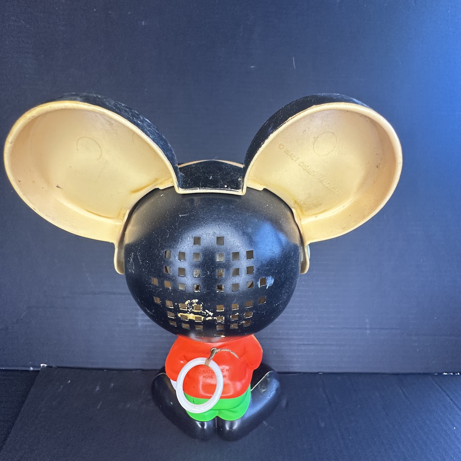 Rear view of a 1970s Mattel pull-string talking Mickey Mouse plastic toy showing black head with speaker grille, rounded ears, red shirt, green pants, and white pull-ring string