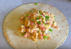 Trải bánh mì tròn hay còn gọi là Tortilla lên thớt hoặc dĩa. Sau đó cho hỗn hợp trứng thịt vào giữa bánh rồi trải đều 60 gram phô mai nhuyễn lên mặt. Sau đó gói bánh lại thật chặt, ôm hết phần nhân.