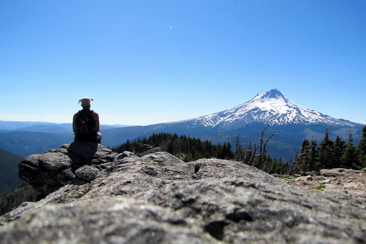 Hiker on a rocky summit looking toward Mount Hood