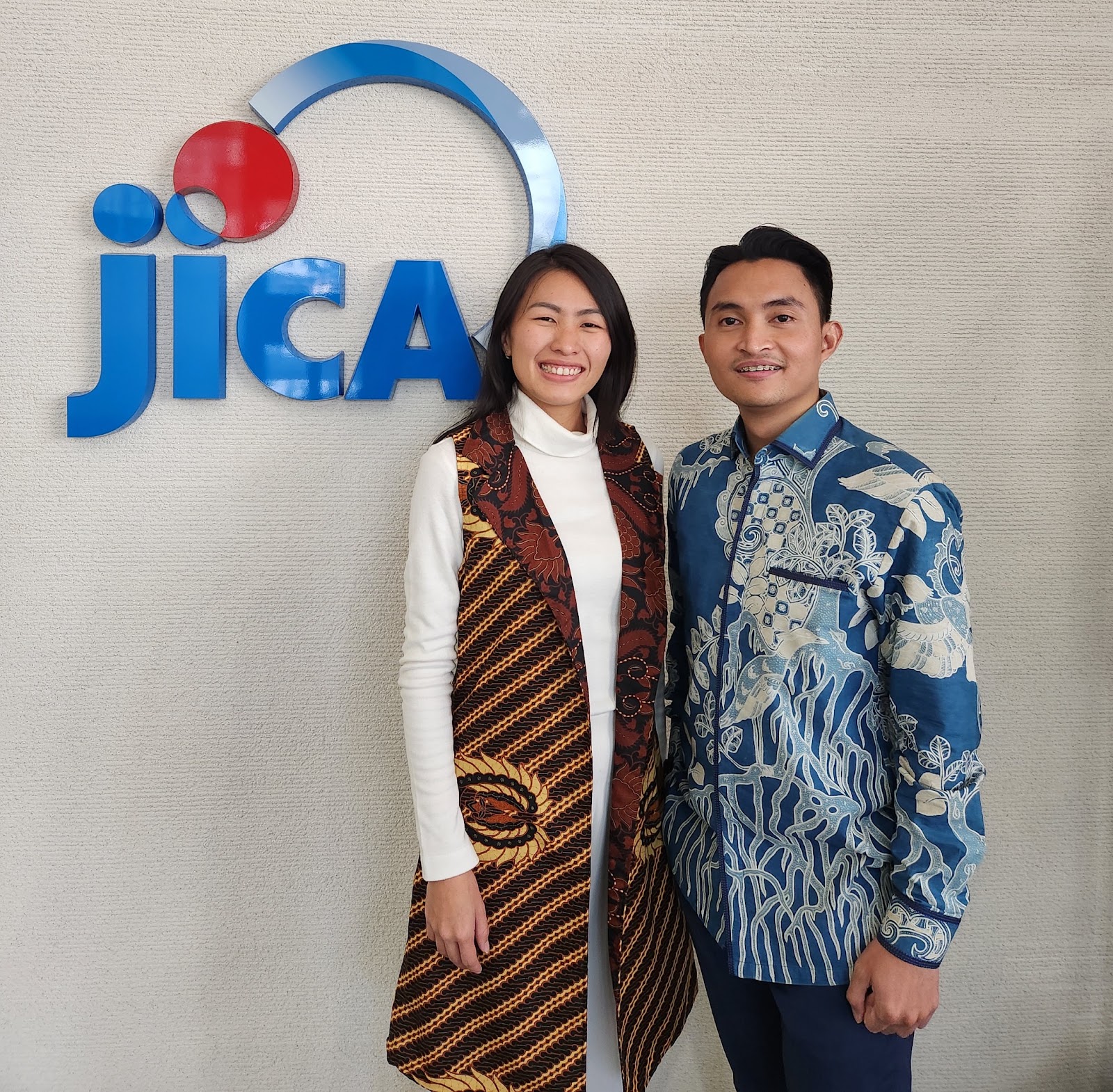Jessica Novia and Agung Bimo Listyanu wearing batik with JICA logo in the background