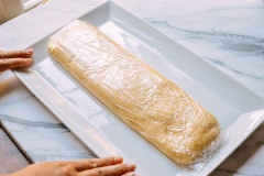 Cho 240g bột mì, trứng gà, 1/2 muỗng muối, 1.5 muỗng bột nở, 1 muỗng sữa tươi, 2 muỗng bơ và dùng máy trộn đều đến khi thành khối bột dẻo mịn, mượt rồi để bột nghỉ 15 phút. Lấy bột ra, tạo thành hình chữ nhật dài rồi bọc màng bọc lại, cho vào tủ lạnh để qua đêm. Hôm sau lấy bột ra, để bên ngoài 1 - 2 tiếng cho mềm hẳn trước khi làm nhé.