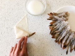 Dùng bột bắp pha với 1/2 chén nước để làm "keo" kết dính dán chắt vỏ bánh. Trải miếng bánh pía lên bàn, để theo hình tam giác. Cho 1 con tôm lên trên bánh pía. Phần đuôi quay ra bên ngoài. Quấn tròn đến 1/2 vòng bánh rồi gập đầu lại.