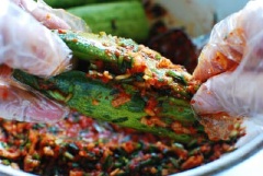 Củ cải trắng băm nhỏ. Hẹ thái nhỏ. Cho hẹ, củ cải vào tô trộn với 5 muỗng canh ớt bột, 2 muỗng canh muối tôm Hàn, 1 muỗng tỏi băm, 1 muỗng cà phê gừng băm và 2 muỗng cà phê đường rồi trộn đều tất cả. Dưa leo sau khi ngâm lấy ra khía một đường dọc ngay thân dưa sâu 1cm. Đeo beo tay rồi cho dưa vào gia vị, thoa kĩ và đều để gia vị thấm vào dưa rồi cho dưa đã muối vào hộp, đậy kín khoảng 1 ngày là có thể dùng được.