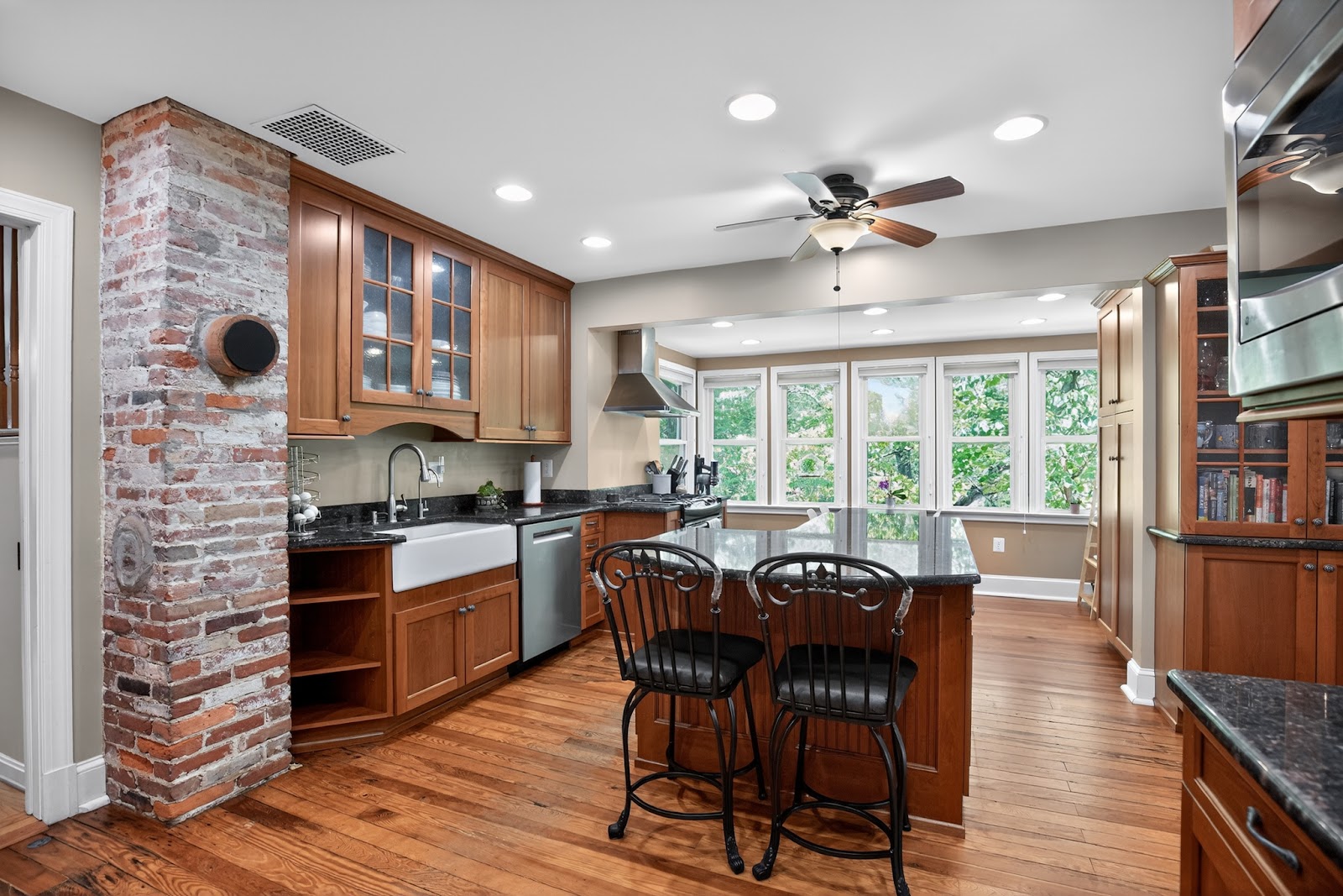 Warm traditional kitchen with cherry wood cabinetry, exposed brick column, kitchen island with bar seating, and farmhouse sink — older South Jersey home with great bones