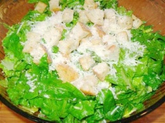 Cách làm salad: Rau xà lách xắt nhỏ rồi cho vào tô. Thêm 1/2 chỗ bánh mì nướng, rắc 1/2 phô mai chỗ Parmesan bào vụn lên và trộn đều lên.
