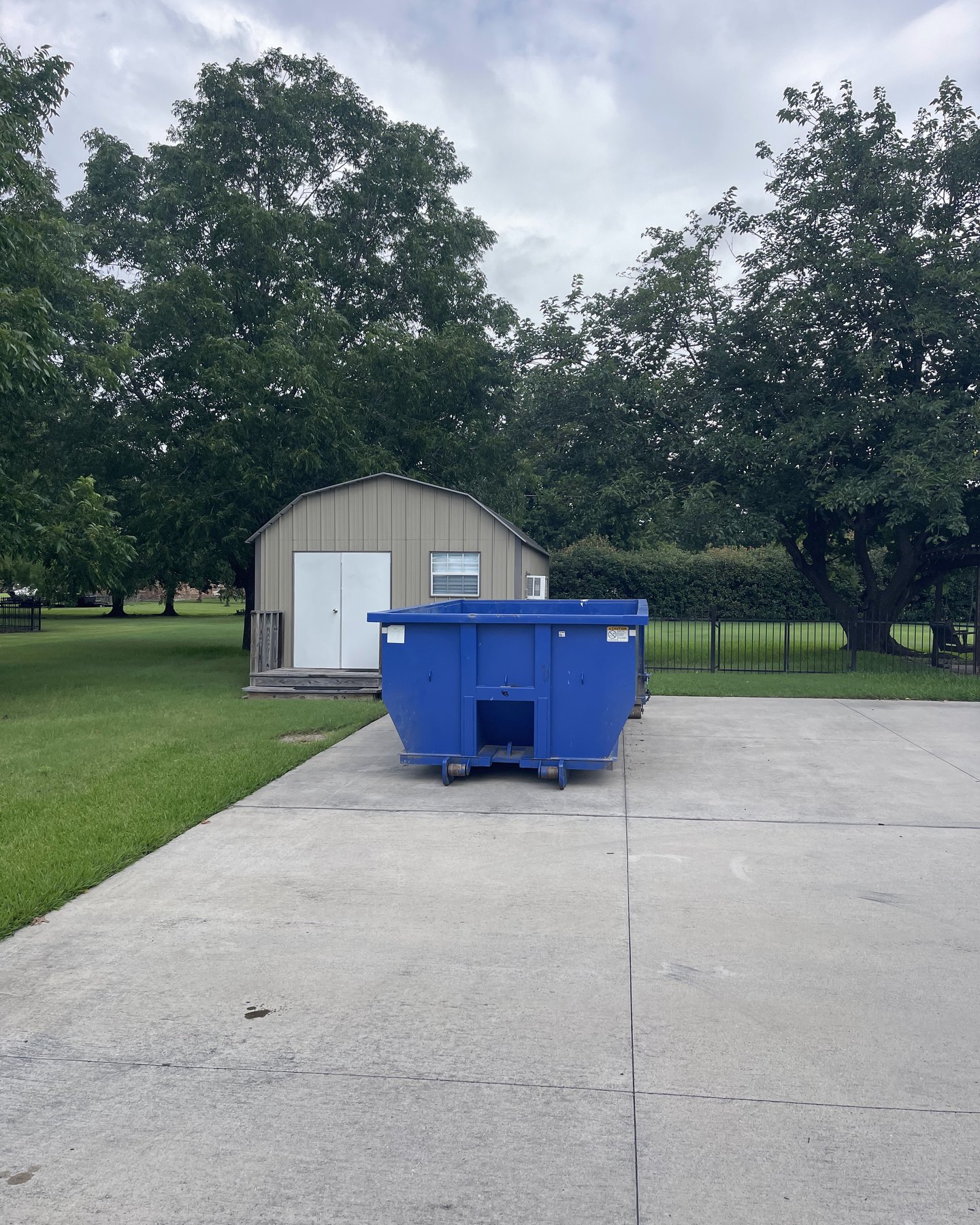 Roll-off dumpster by a backyard shed for a property cleanout