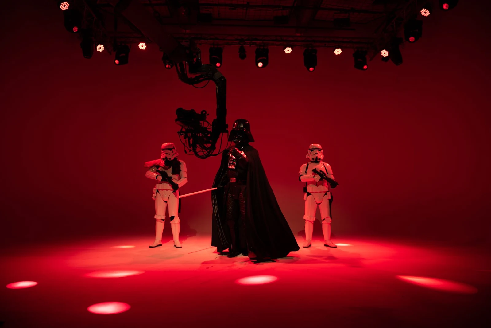 Three sci-fi characters in costumes pose under red studio lights, creating a dramatic scene.