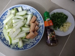 Bào vỏ bầu, rửa sạch nhựa, cắt khoanh dày 1cm, sau đó cắt thanh dày 1.5cm. Bỏ gốc hành lá và ngò rí, rửa sạch cắt khúc 2cm. Cắt mỗi cây xúc xích làm 2 phần, sau đó chẻ dọc chia làm 4 dài 1/2 chiều dài xúc xích (sau khi chiên xúc xích sẽ bung ra như hoa)