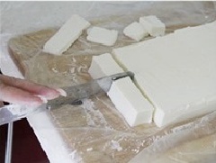 Khi hỗn hợp đã đông lại, bạn cẩn thận lấy ra và dùng dao cắt đi phần góc (để đẹp mắt) rồi cắt thành từng thanh với chiều rộng tầm 2cm. Tiếp tục cắt thành miếng vuông nhỏ và lăn qua một lớp vụn dừa khô. Vậy là chúng ta đã hoàn thành món bánh sữa dừa thơm ngon rồi đấy!