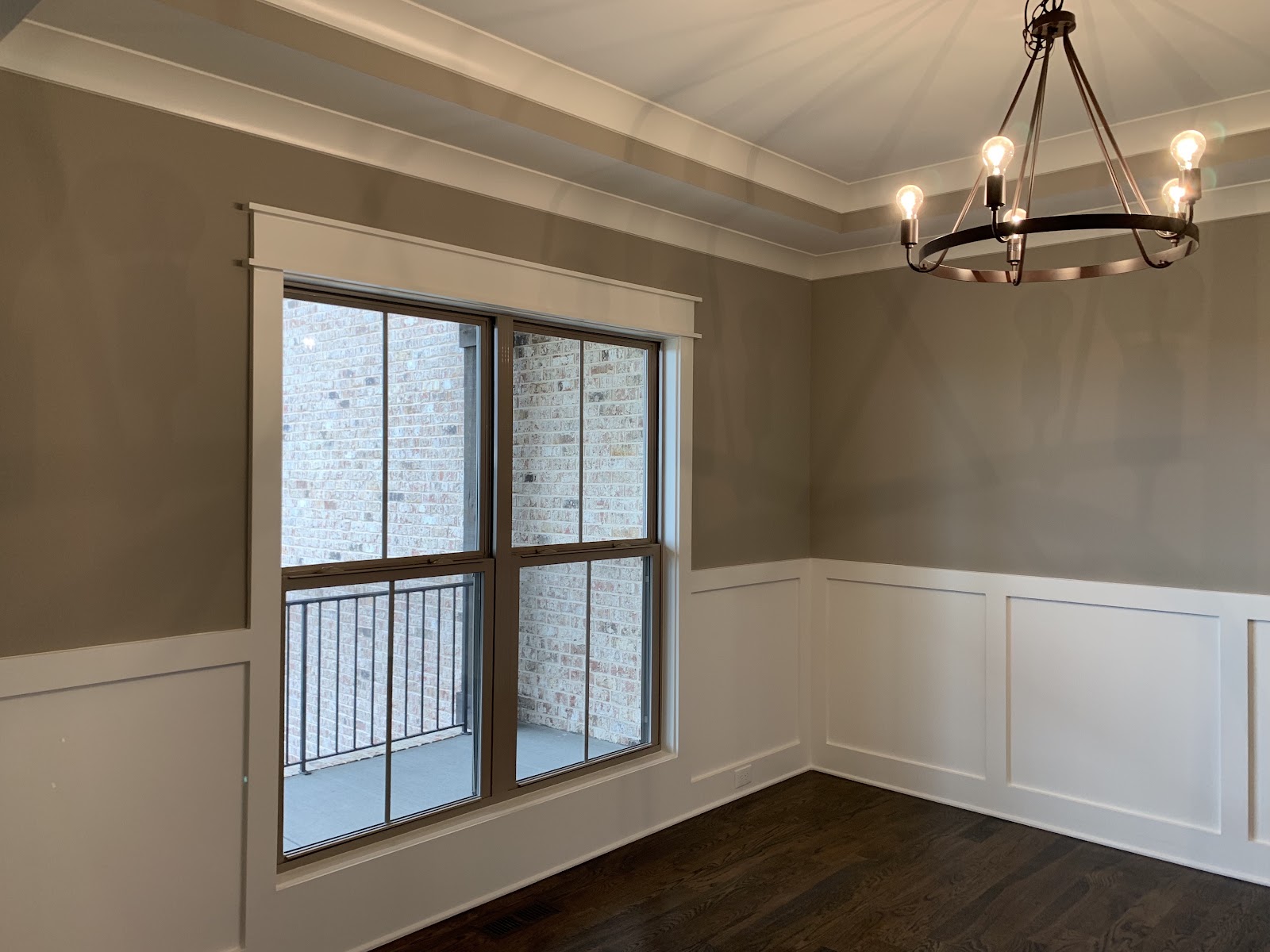 Room with dark wood floors, grey walls, white wainscoting, a tray ceiling, and a dark metal chandelier.