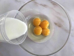 Tách lấy 4 lòng đỏ trứng gà cho vào tô, thêm vào 50g dầu bắp, 80ml sữa tươi nguyên chất, dùng phới lồng đánh tan đều.