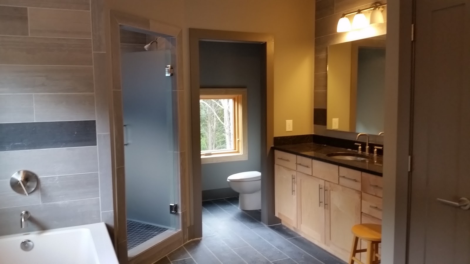 Bathroom interior with a double vanity, tiled walls, a glass-enclosed shower, and a separate toilet area visible through a doorway.