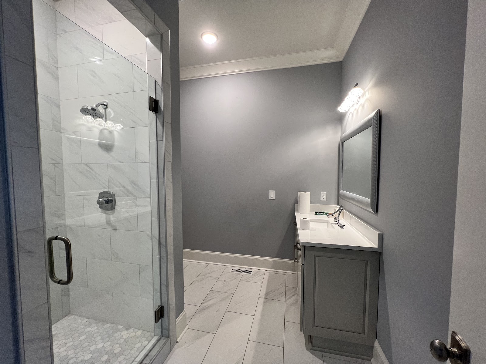 Interior of a Middle Tennessee residence with a glass-enclosed shower, grey vanity, white countertop, and marble-patterned tile flooring.